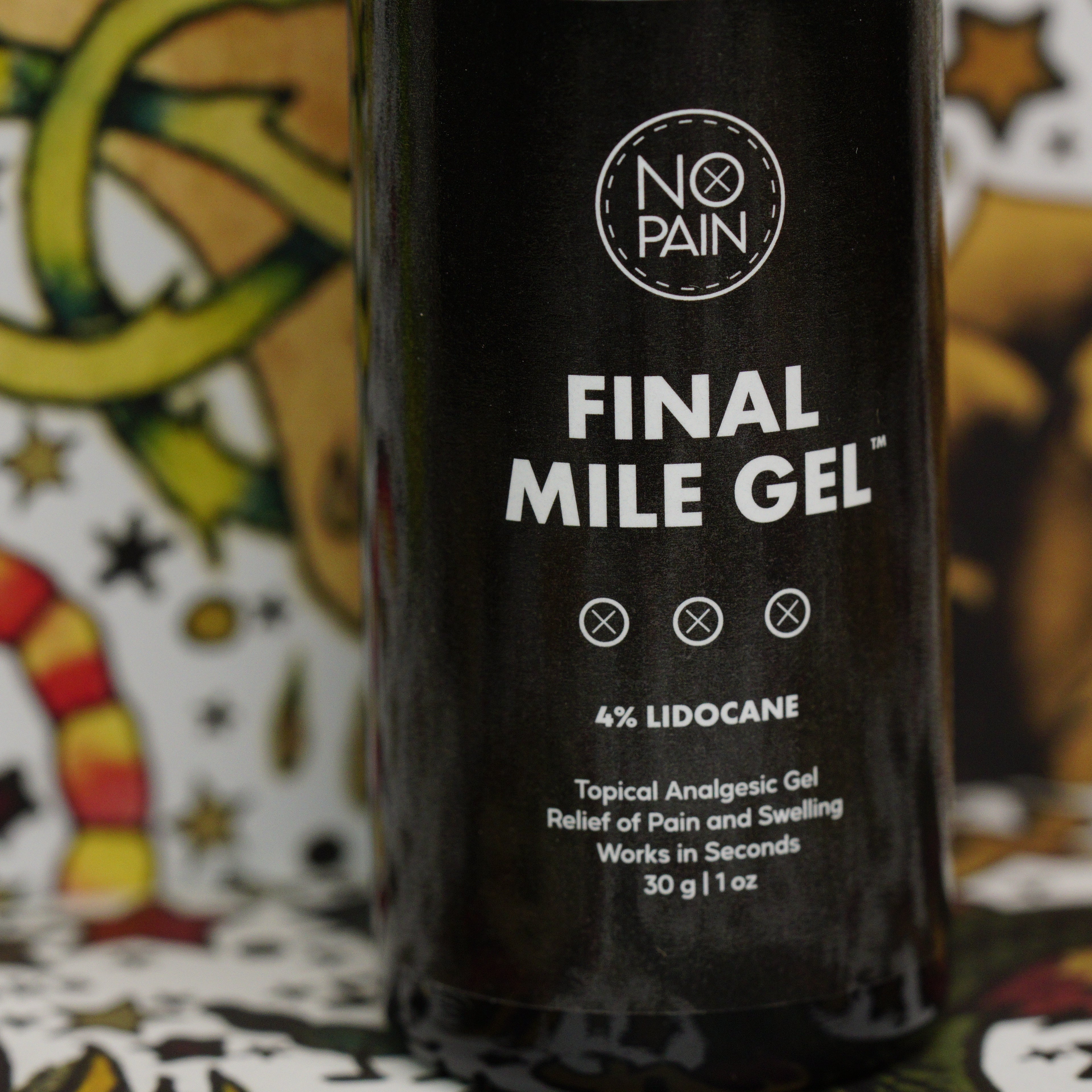 A close-up of a product bottle labeled "Final Mile Gelâ„¢" from No Pain Tattoo LLC shows details of "4% Lidocaine" and "Topical Analgesic Gel - Relief of Pain and Swelling - Works in Seconds - 30g | 1oz." The background features colorful, abstract designs, emphasizing the promise of instant relief provided by Final Mile Gelâ„¢.