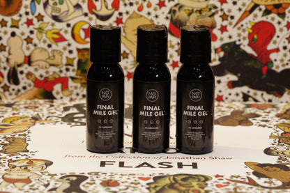 Three sleek black bottles labeled "Final Mile Gel™" from No Pain Tattoo LLC are standing on a decorative surface. The background features colorful, intricate cartoon drawings, with text below the bottles reading "from the Collection of Jonathan Shaw - FLASH." Infused with a lidocaine formula, this gel ensures no pain during your final mile.