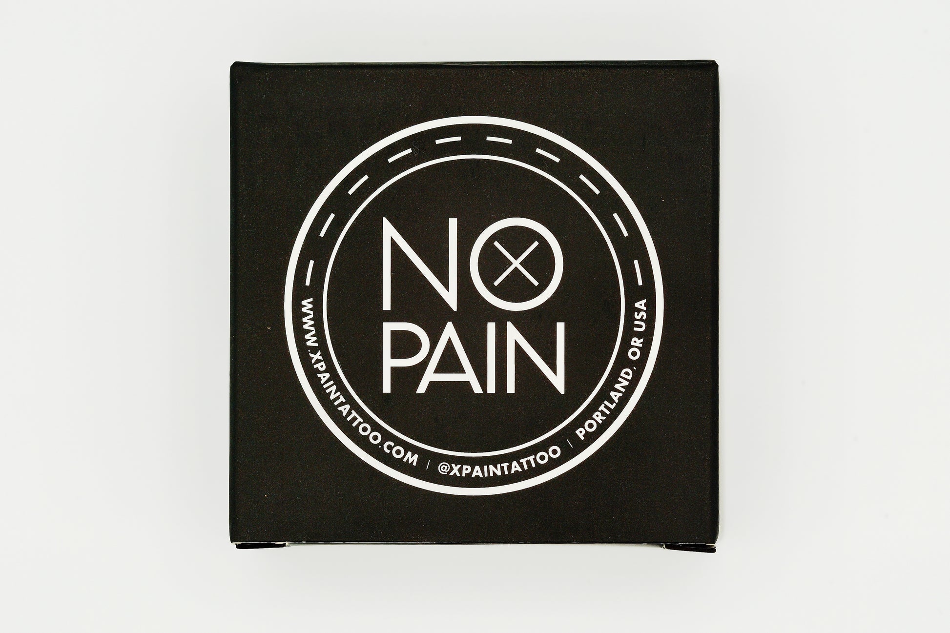 A black square box with a white circular logo on top features the words "NO PAIN" in large letters, emphasizing its role in rapid healing. The border of the circle includes the website "www.xpaintattoo.com" and the location "Portland, OR USA". Perfect for My Store's No Pain Tattoo Aftercare Balm 30g to heal professional tattoos.