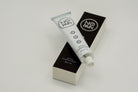 A white tube labeled "No Pain Tattoo Numbing Cream" rests on its black and white packaging box. The tube features a small open cap and displays product details, including "30g | 1 oz," along with symbols indicating it is designed for pain-free tattooing.